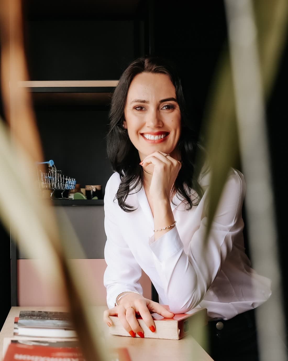 Rafaela Poleza sorrindo, com a mão no queixo, apoiada sobre livros em uma mesa.